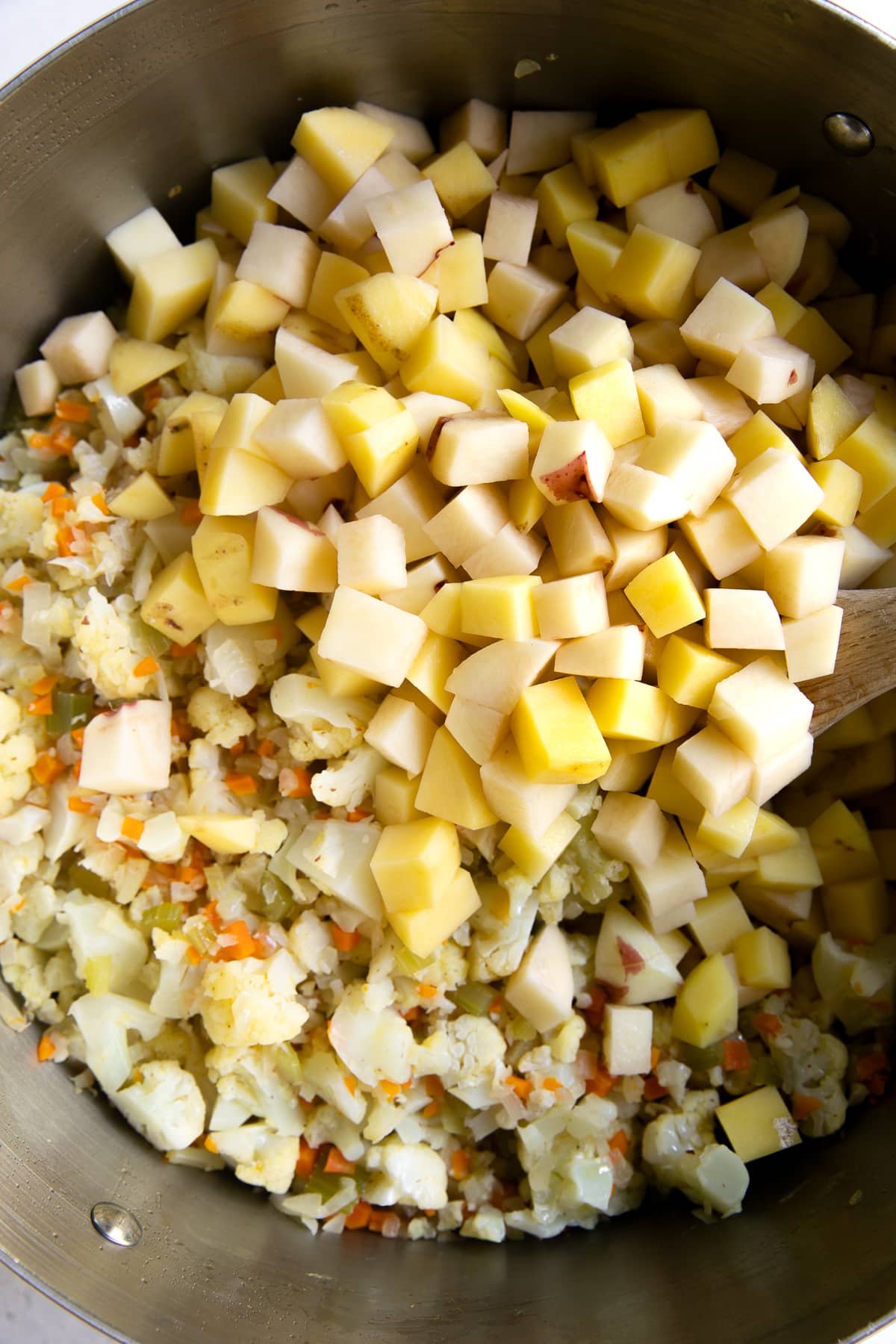 Finely minced onion, celery, and carrots, cooking in a large pot with finely chopped cauliflower and diced potatoes.