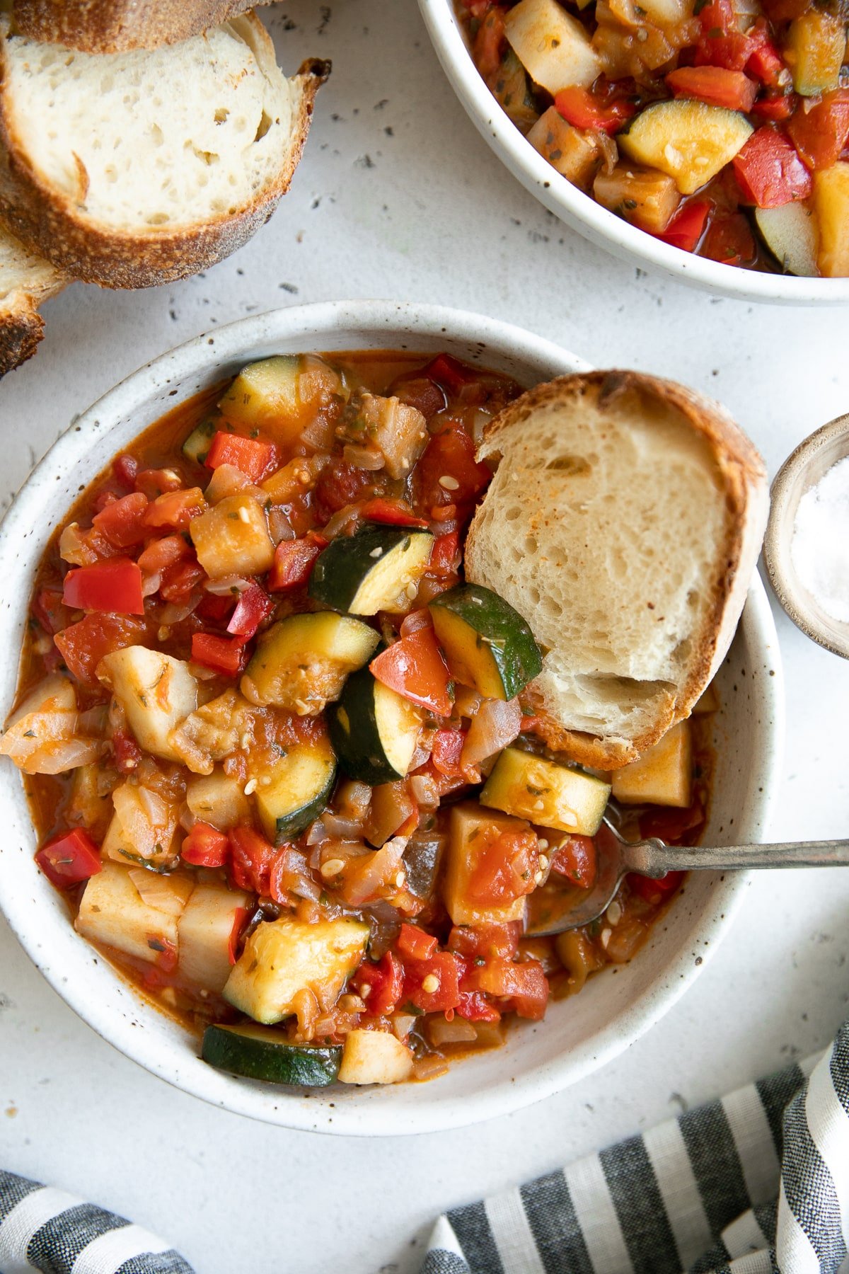 White shallow bowl filled with homemade ciambotta and served with fresh toasted bread.