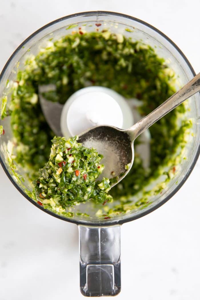 Small food processor filled with blended pestata made from olive oil, fresh oregano, basil, garlic, and red pepper flakes.