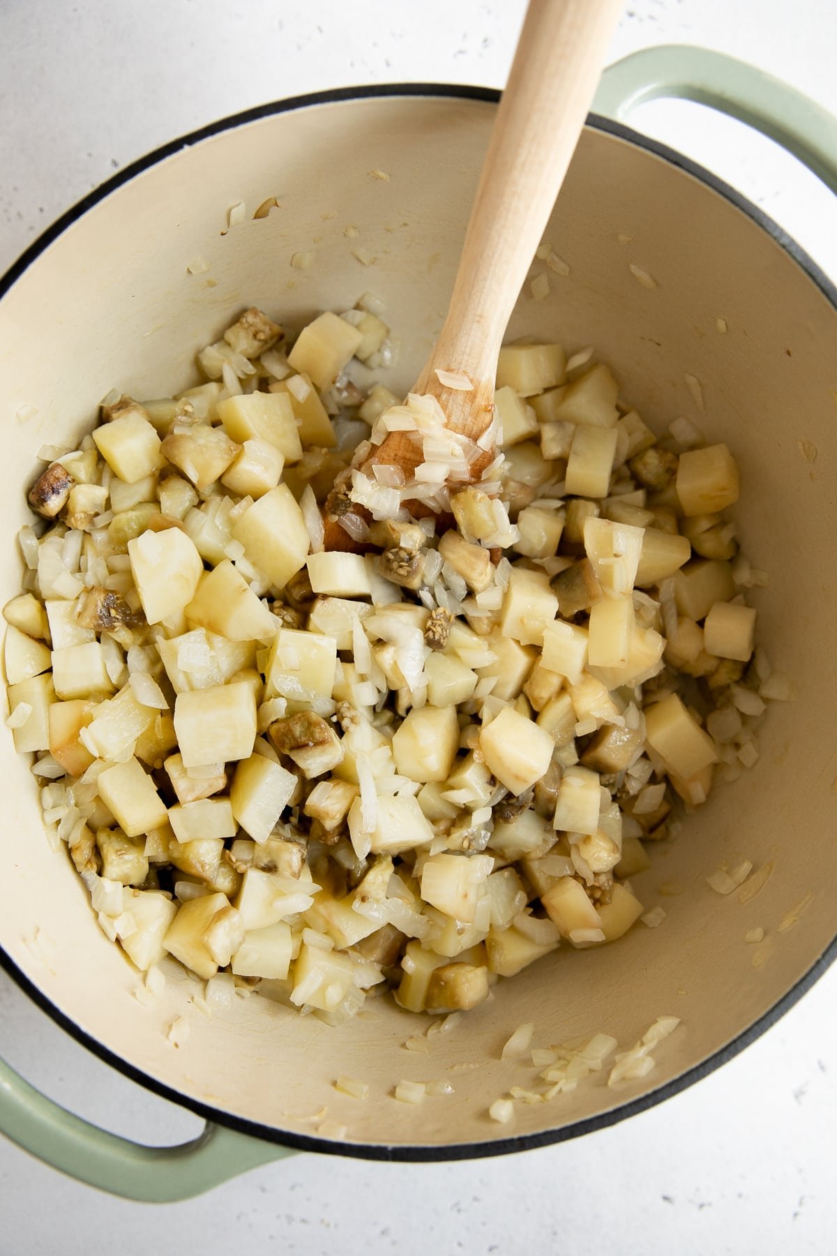 Chopped potatoes, eggplant, and onions sauteing in a large Dutch oven.