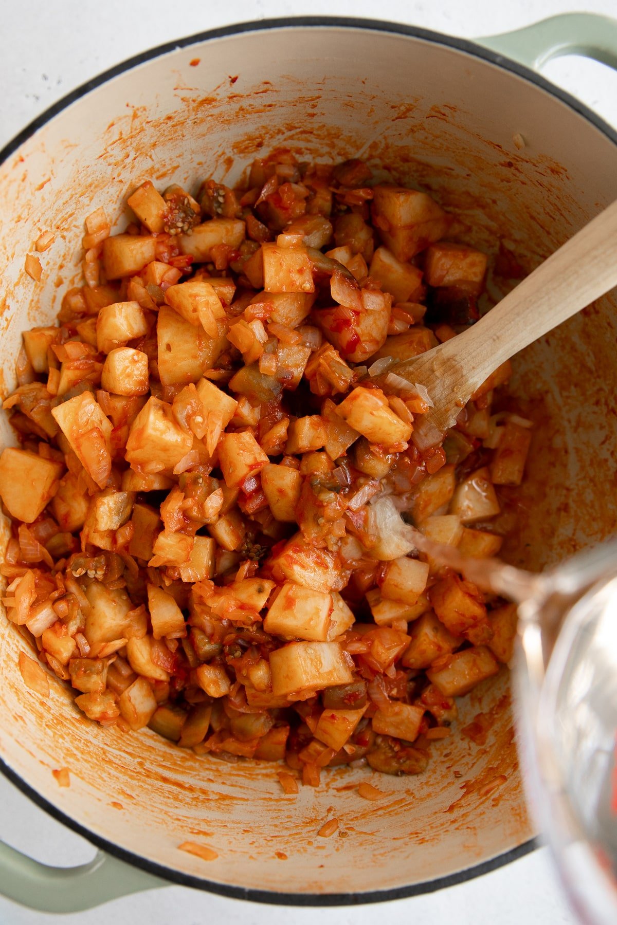 Adding water to cooking potatoes and tomatoes in a large Dutch oven.