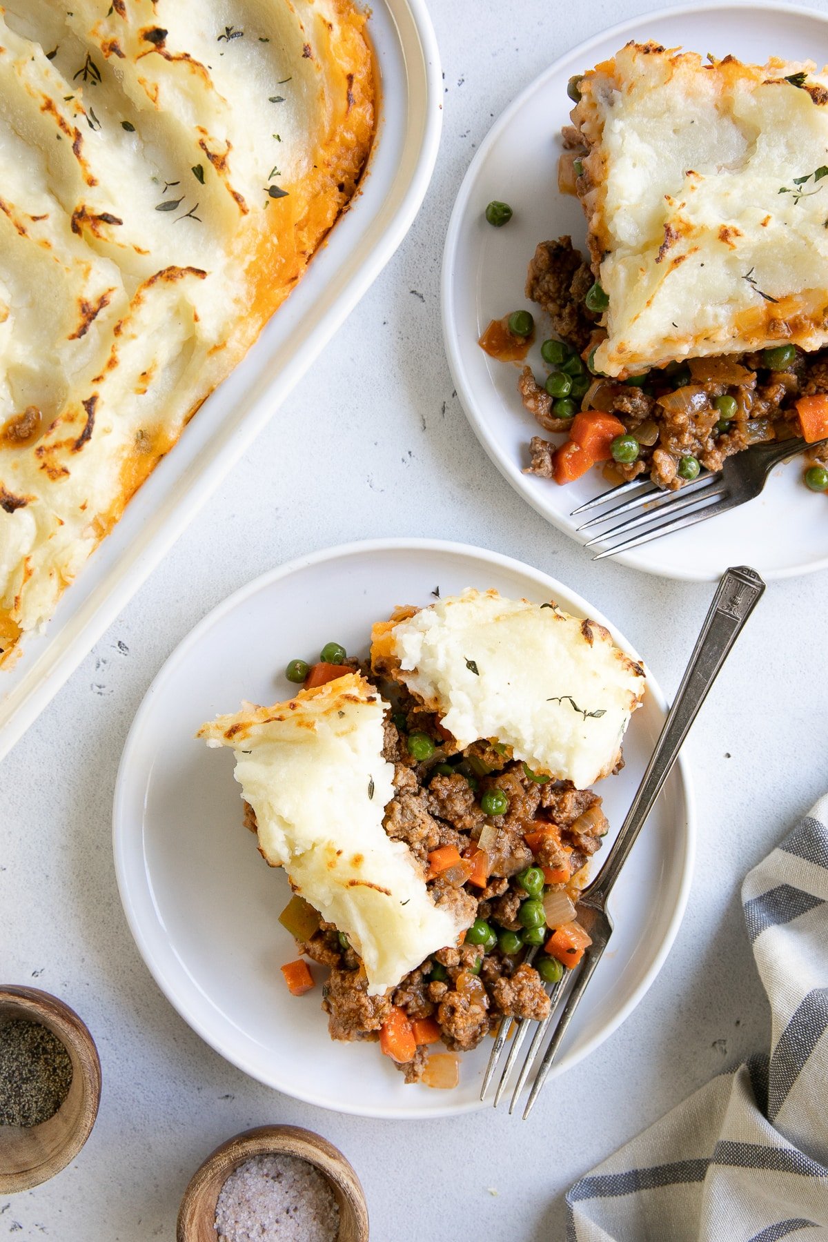 Two white serving plates with a big slice of homemade classic shepherd's pie.