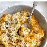 Bowl of creamy butternut squash risotto topped with grated parmesan cheese and herbs, with a spoon resting in the bowl.