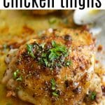 Close-up of a golden, juicy baked chicken thigh topped with chopped fresh herbs, sitting on a baking sheet with flavorful juices.