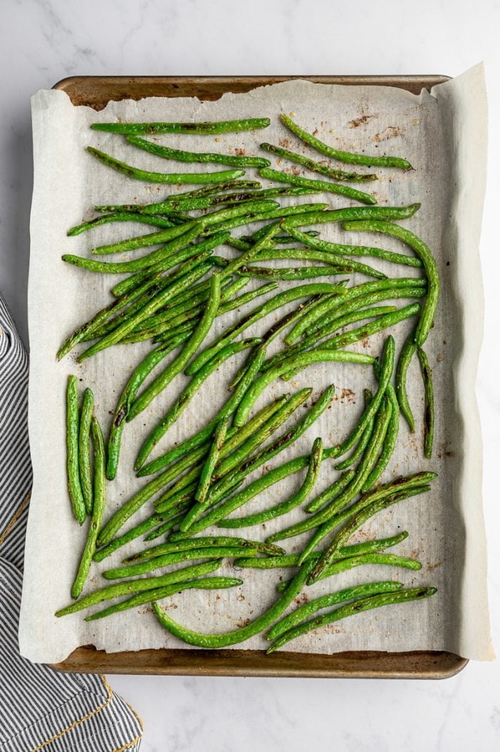 Oven roasted green beans with browned spots on a parchment-lined baking sheet