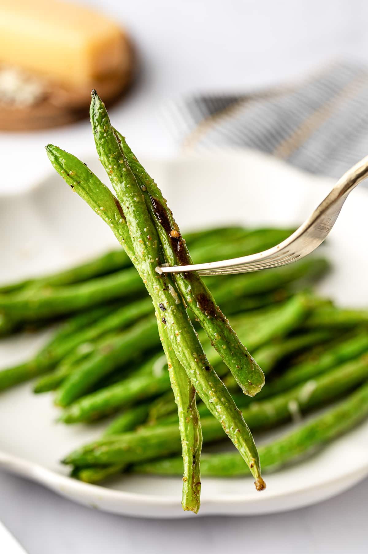 Fork holding several roasted green beans above a plate