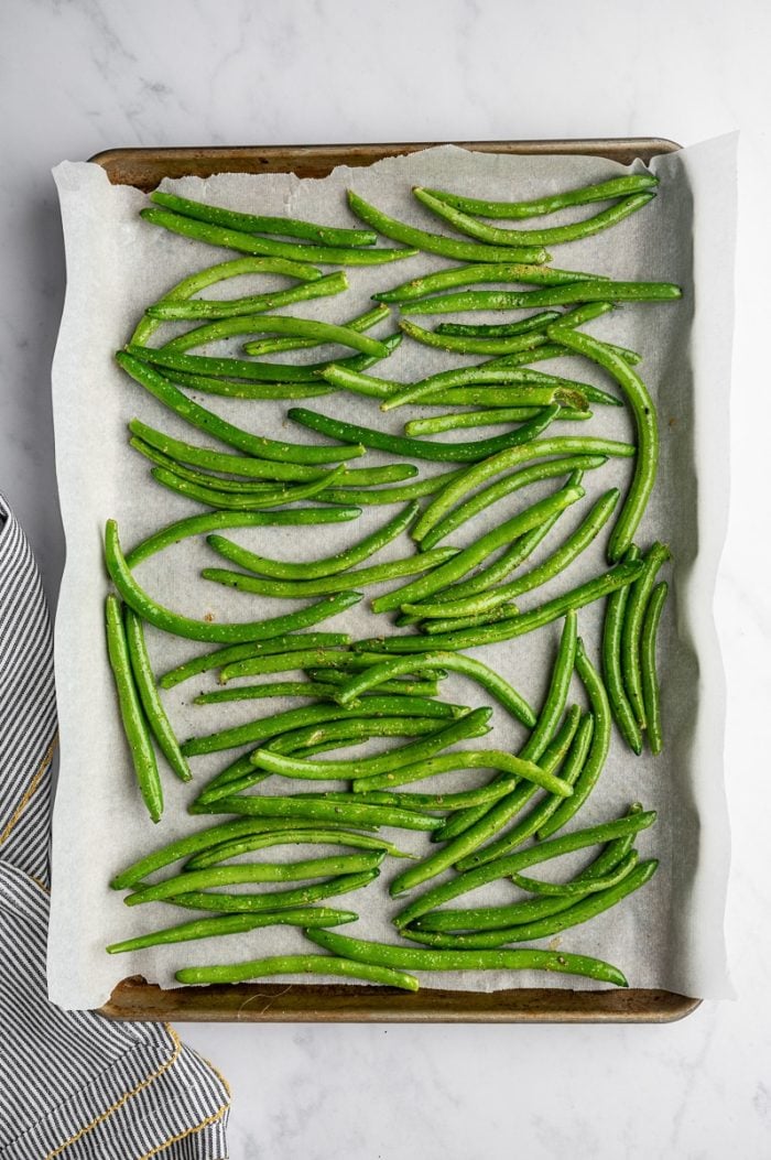 Seasoned green beans arranged in a single layer on a parchment-lined baking sheet