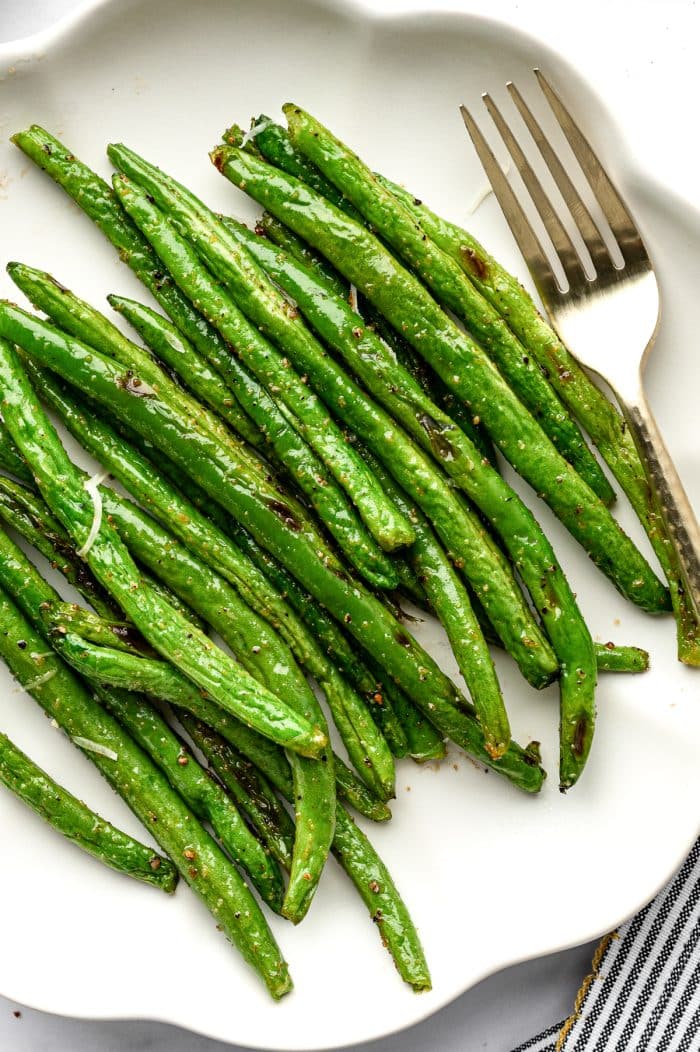 Close up of roasted green beans on a white serving plate with a fork