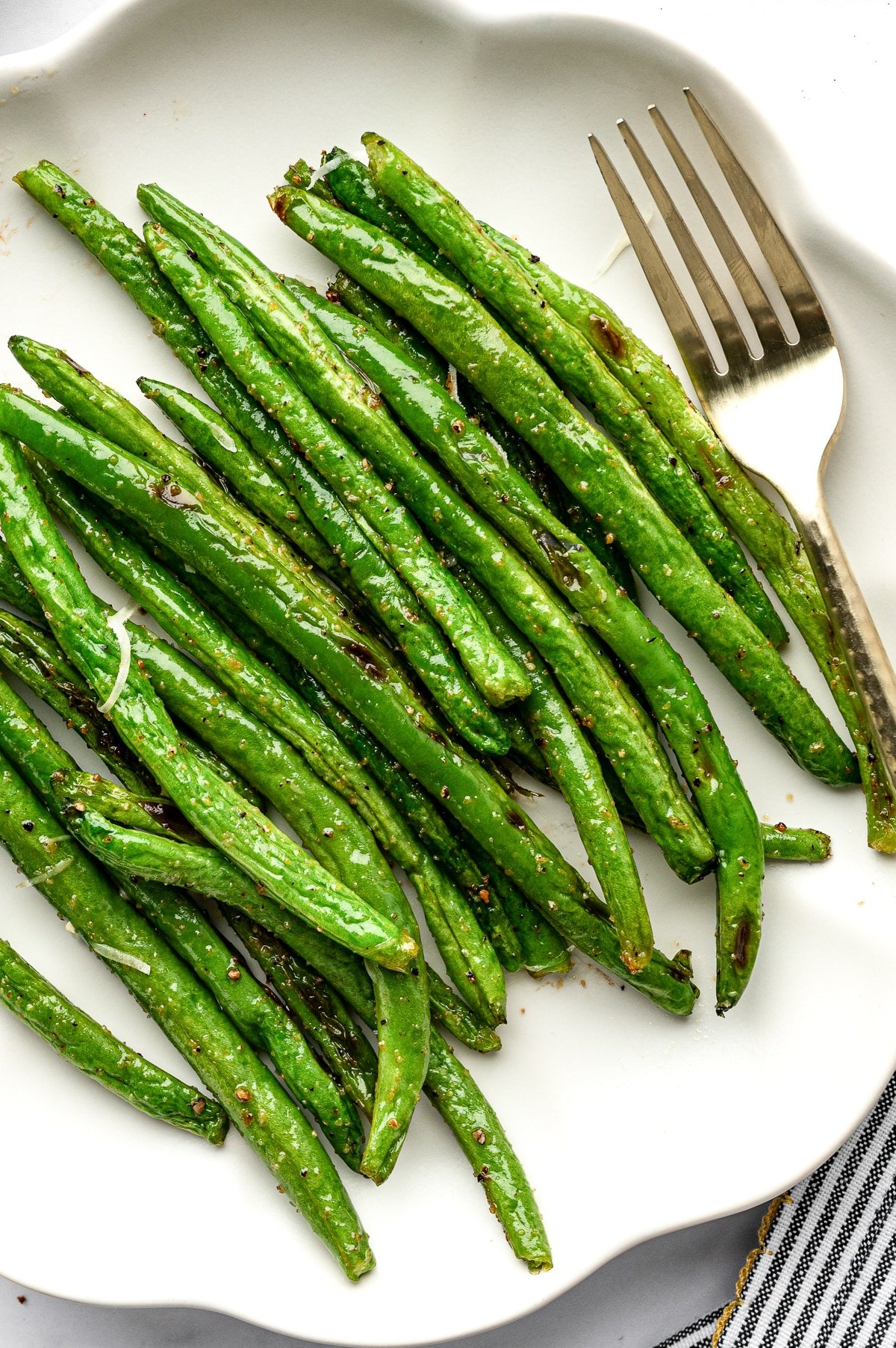 Close up of roasted green beans on a white serving plate with a fork