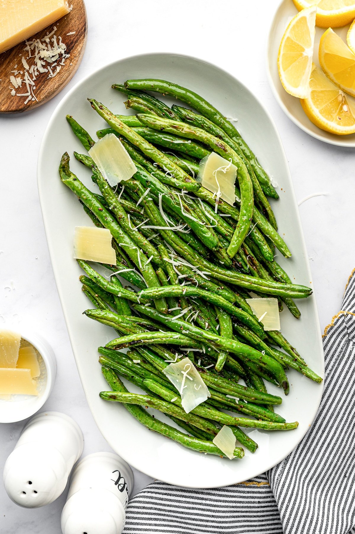 Platter of roasted green beans topped with Parmesan shavings and served with lemon wedges