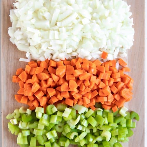 Cutting board with finely chopped onion, carrots, and celery.