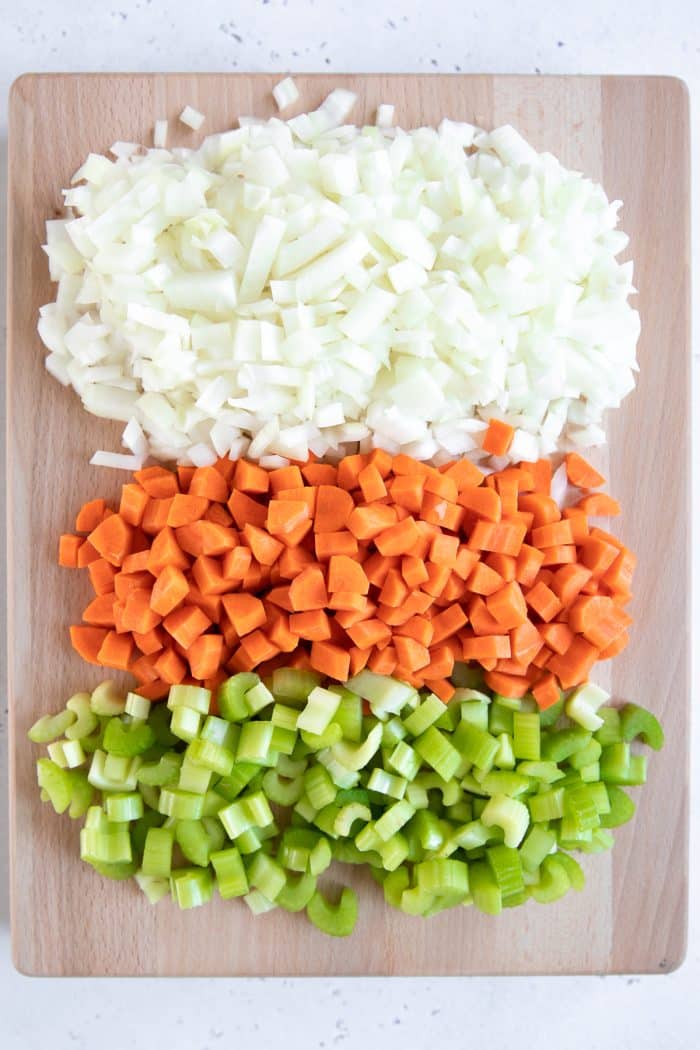 Cutting board with finely chopped onion, carrots, and celery.