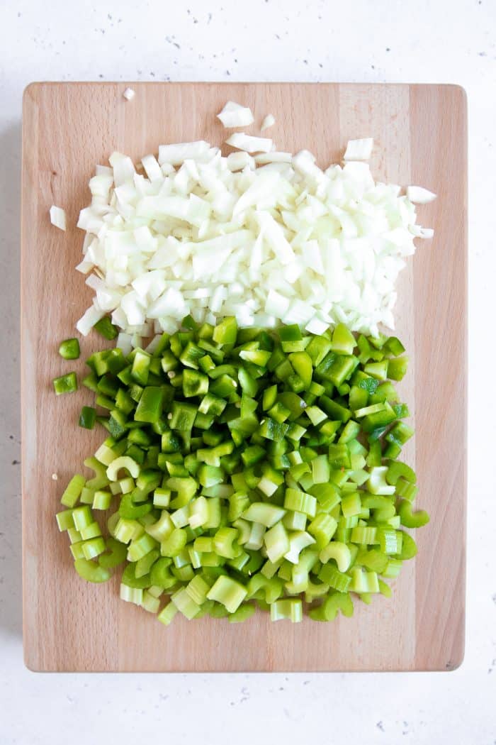 Cutting board with equal amounts of onion, green bell pepper, and celery, also known as the holy trinity.