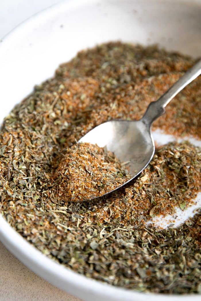 Bowl and spoon filled with a spoonful of homemade poultry seasoning.