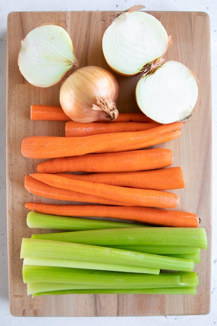 Cutting board with celery, carrots, and whole onions.