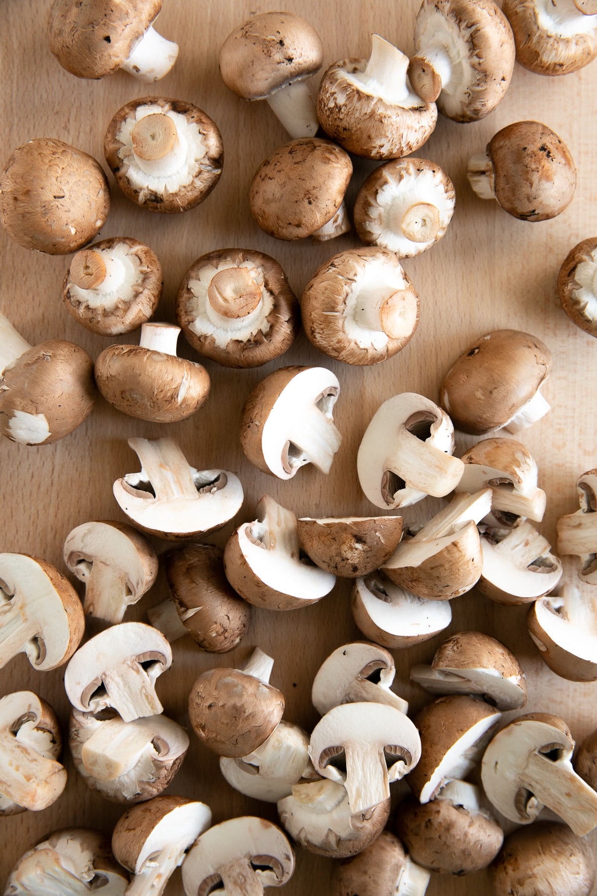 Raw crimini mushrooms sliced in half on a cutting board.