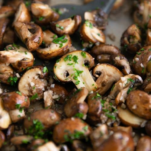 Mushrooms sauteeing in a large skillet with butter and garlic and sprinkled with fresh parsley.