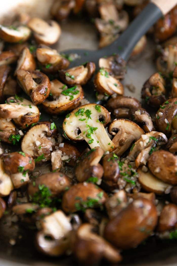 Mushrooms sauteeing in a large skillet with butter and garlic and sprinkled with fresh parsley.