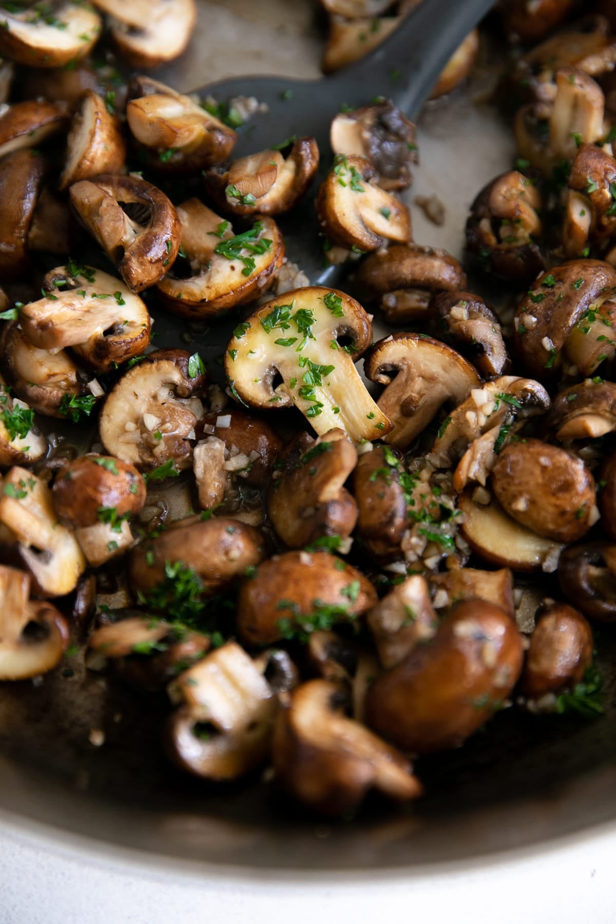 Mushrooms sauteeing in a large skillet with butter and garlic and sprinkled with fresh parsley.