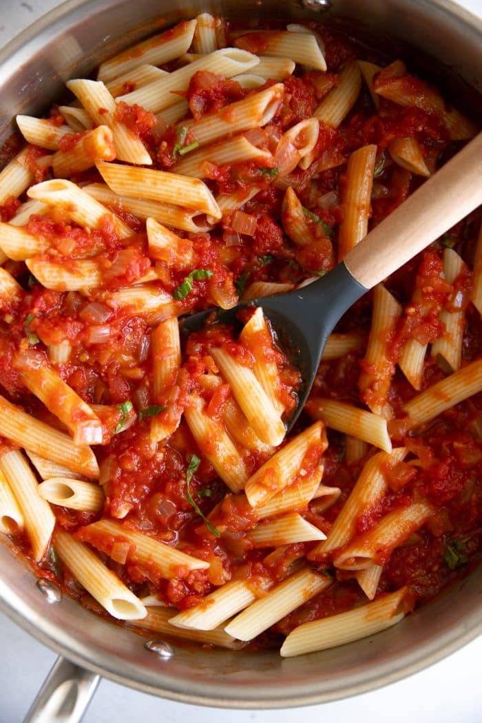 Cooked penne pasta mixed with arrabbiata sauce in a deep pan.