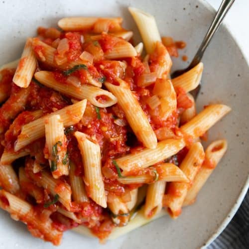 Small dinner plate filled with penne noodles tossed in homemade arrabbiata sauce.