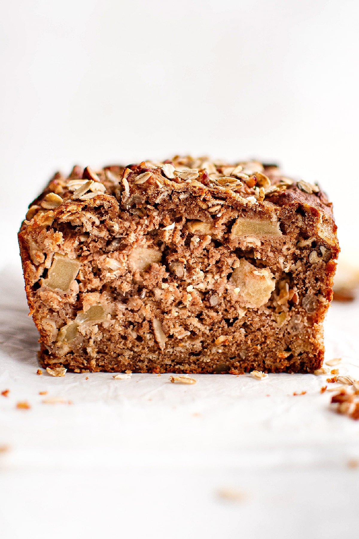 Close-up cross-section of apple cinnamon bread showing a moist, tender interior filled with apple chunks, oats, and chopped nuts.