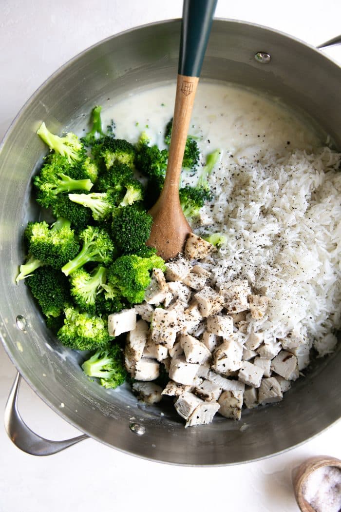 Large pot filled with homemade cream sauce, cooked rice, chicken, and blanched broccoli.