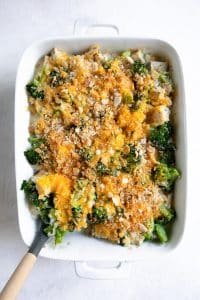 Overhead image of a large white casserole dish filled with creamy baked broccoli, chicken, and rice casserole topped with melted cheddar cheese.