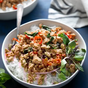 White shallow bowl filled with cooked white rice and topped with prepared thai basil chicken.