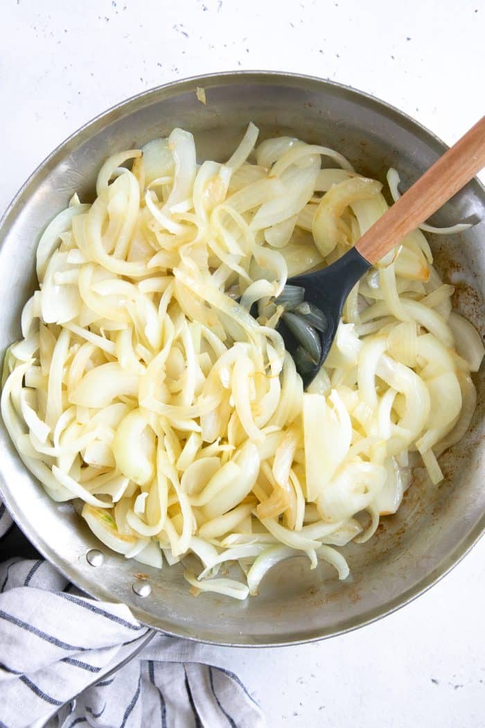 Sliced yellow onions slowly cooking in a medium skillet.