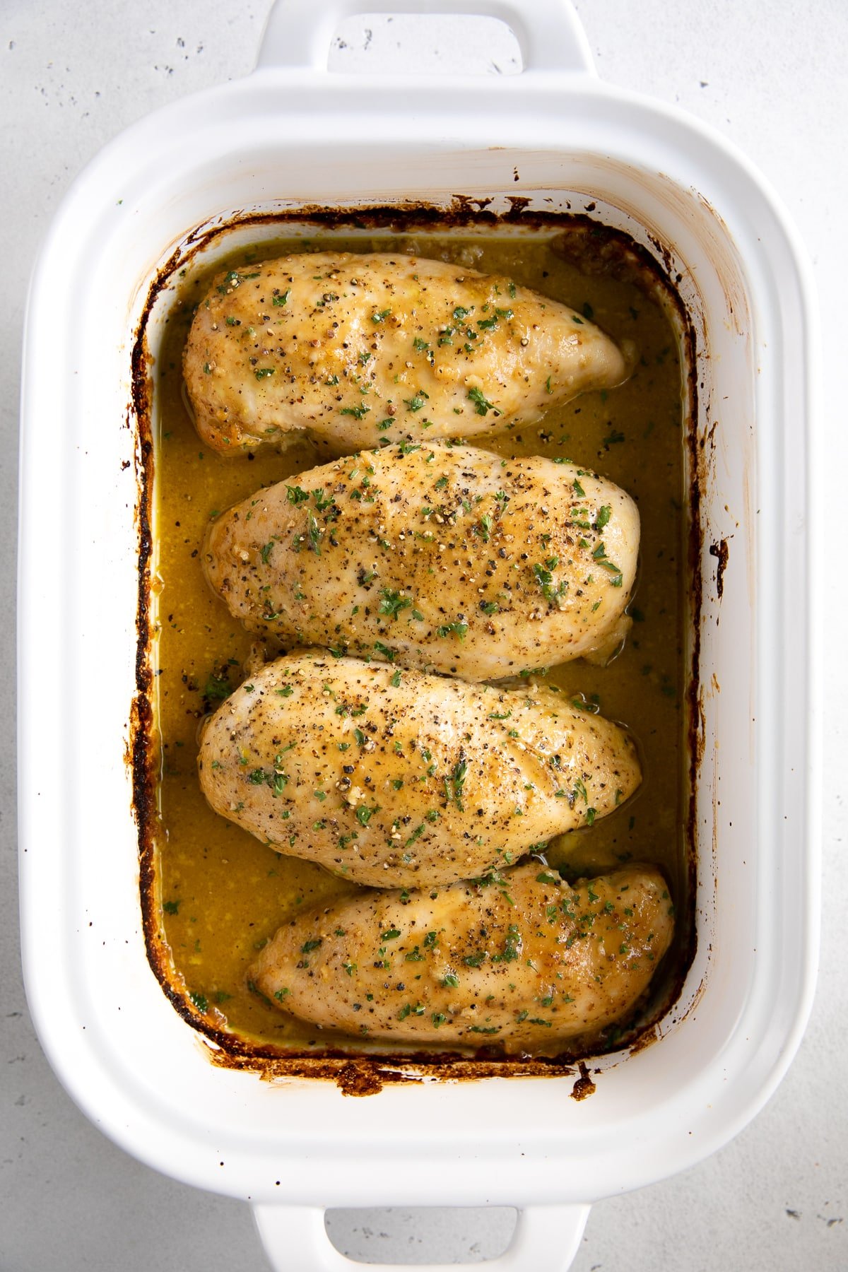 Four large chicken breasts in a white baking dish covered in honey mustard sauce and baked.