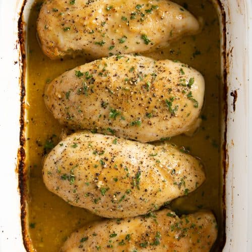 White baking dish filled with four baked chicken breasts covered with homemade honey mustard sauce.