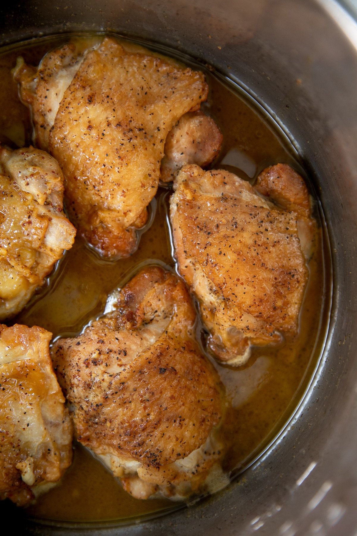 Five cooked chicken thighs in the bowl of a six quart Instant Pot resting in delicious honey mustard sauce.
