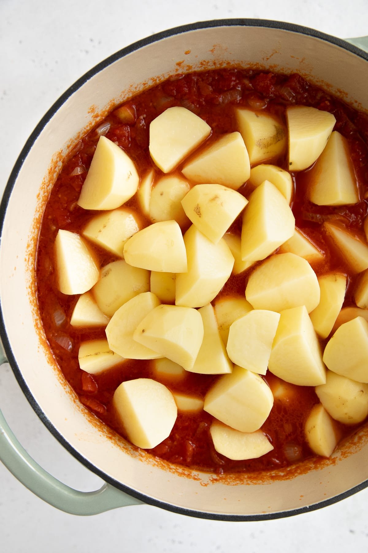 Large Dutch oven filled with tomato base broth and peeled, chopped potatoes.