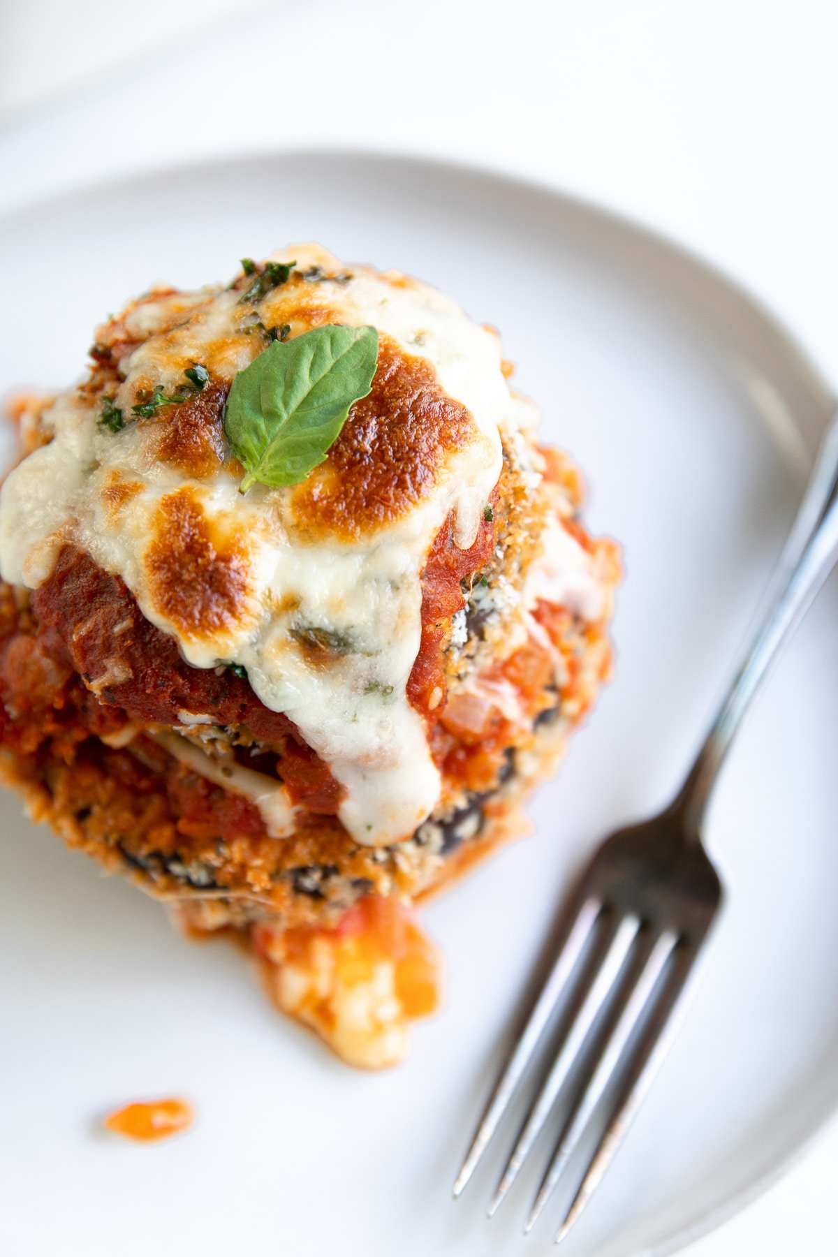 Triple layered baked eggplant parmesan stack on a white plate.