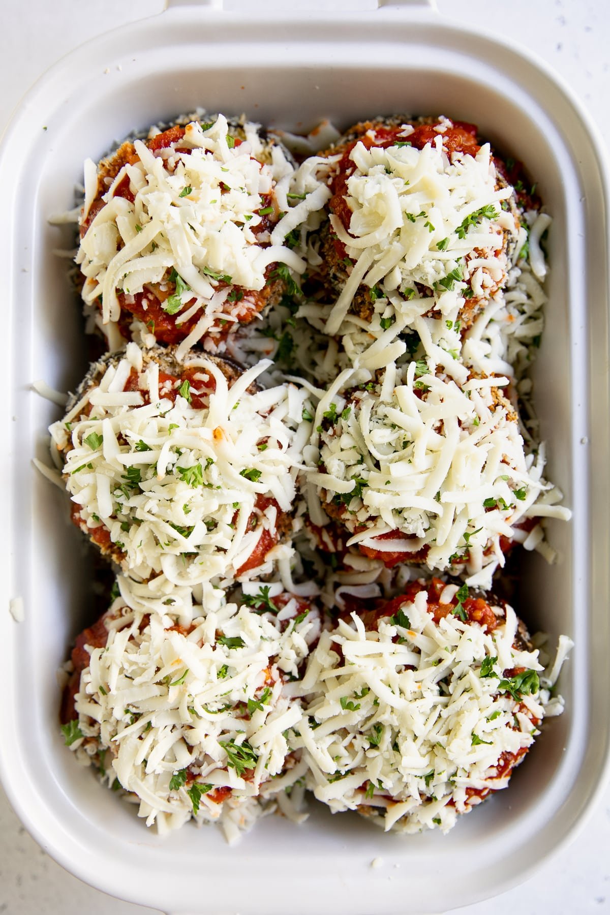 White baking dish filled with three layers of crispy baked eggplant rounds, tomato sauce, and shredded cheese.