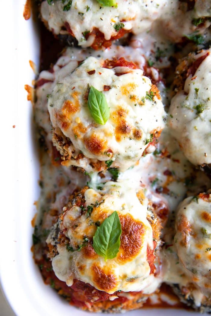 Overhead image of cheesy baked eggplant parmesan stacks topped with a single basil leaf.