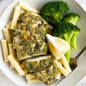 Plate with steamed broccoli, plain boiled pasta noodles, and pesto covered chicken breast.