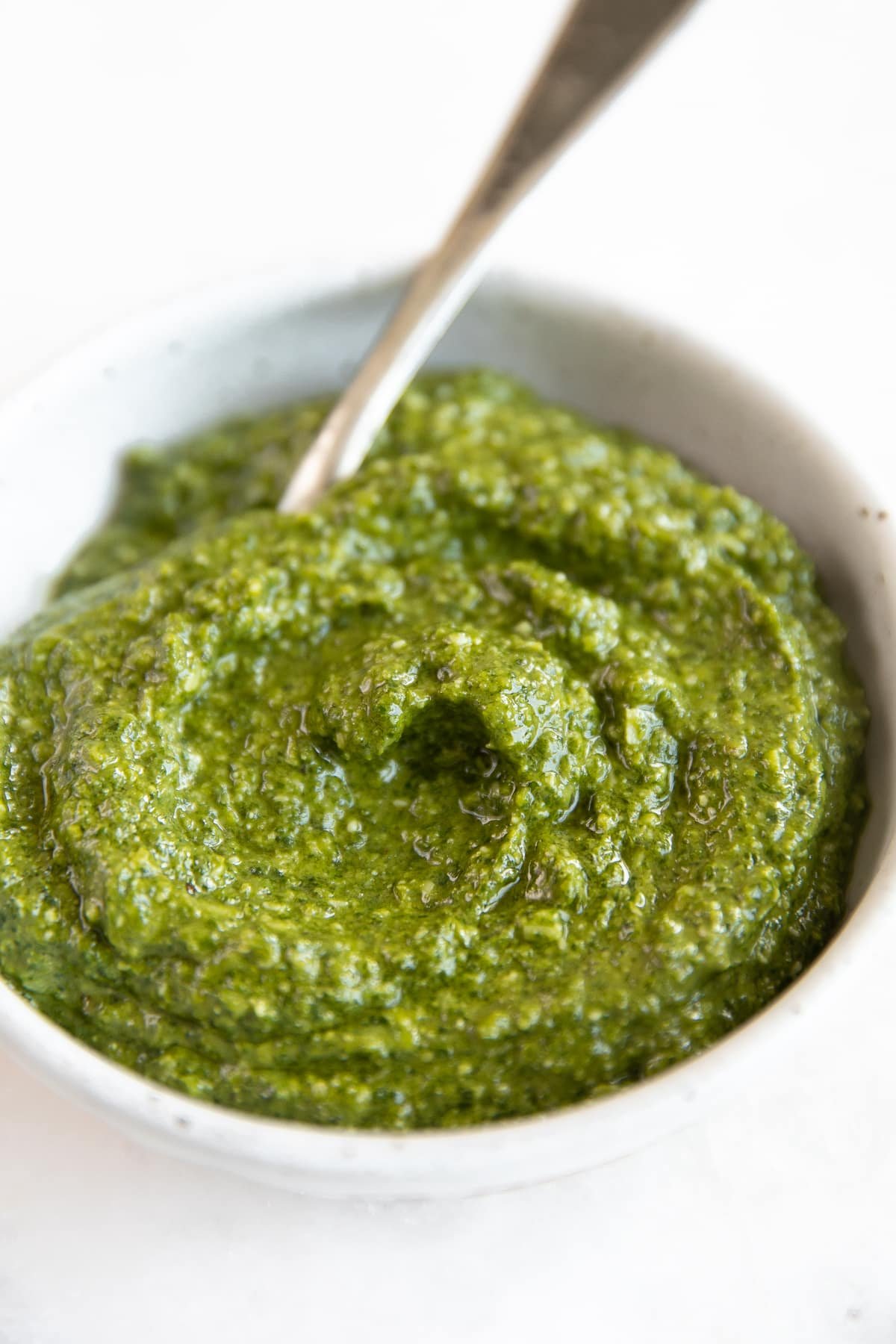 Close up image of freshly processed pesto sauce in a small white bowl.