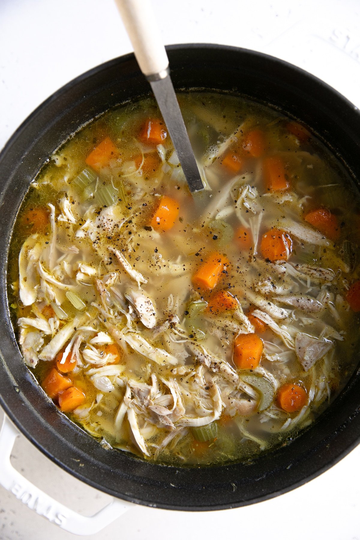 Large white pot filled with homemade chicken soup recipe made with chicken, carrots, celery, and broth.