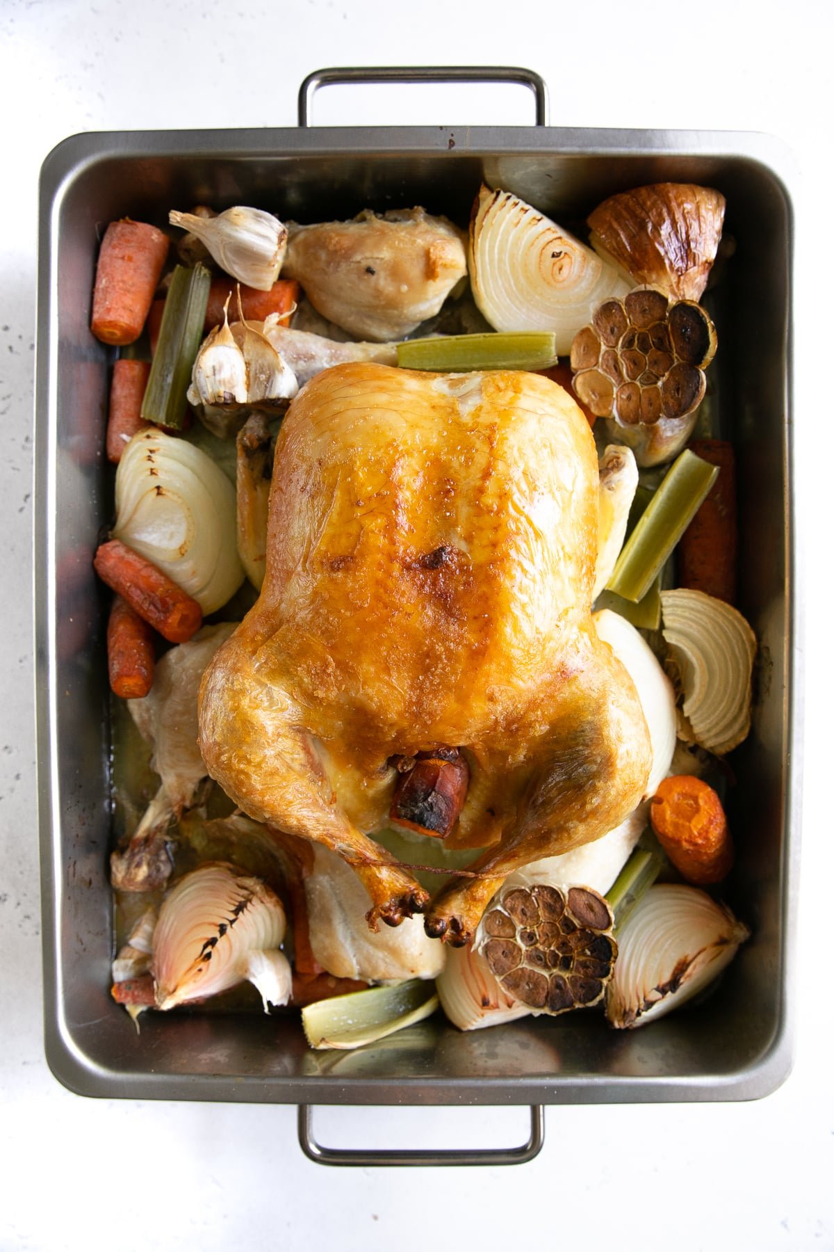 Whole browned chicken and vegetables in a large roasting pan.