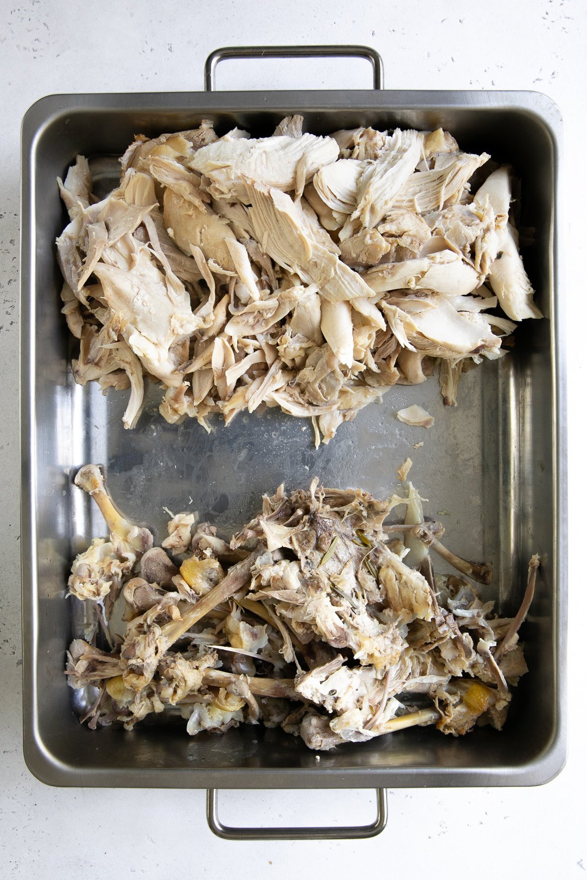 Large roasting pan with shredded chicken on one side and the chicken bones on the other.