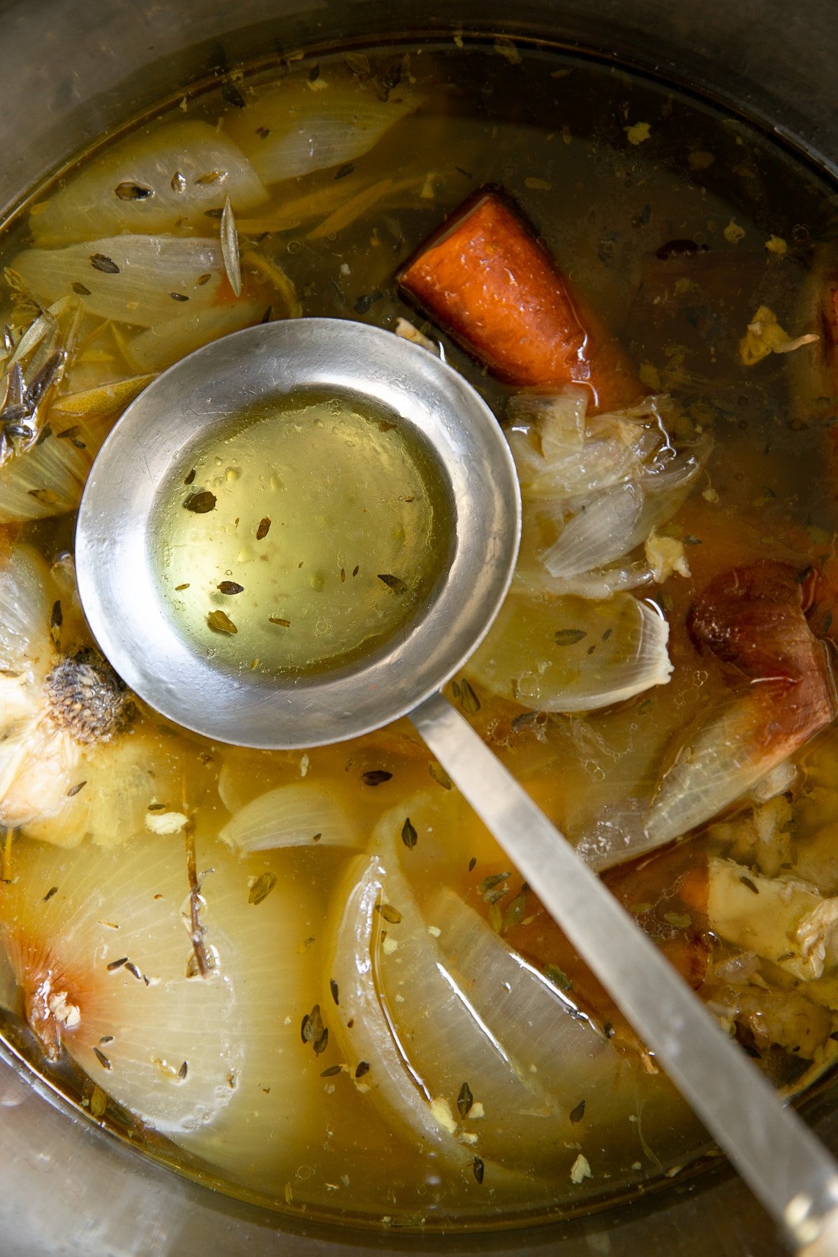 Ladle in a large pot filled with boiled chicken stock and roasting vegetables.