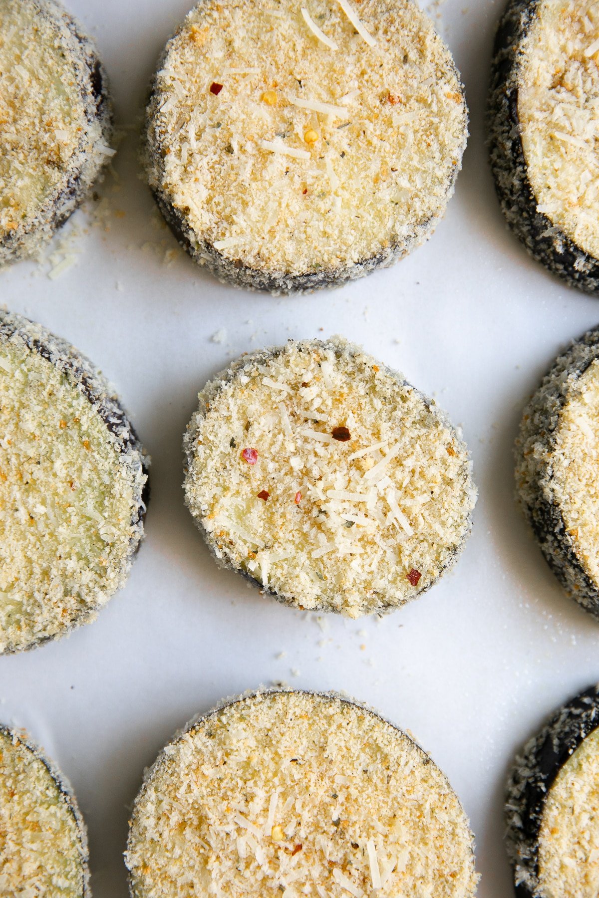 Breaded sliced eggplant on a parchment-lined baking sheet.