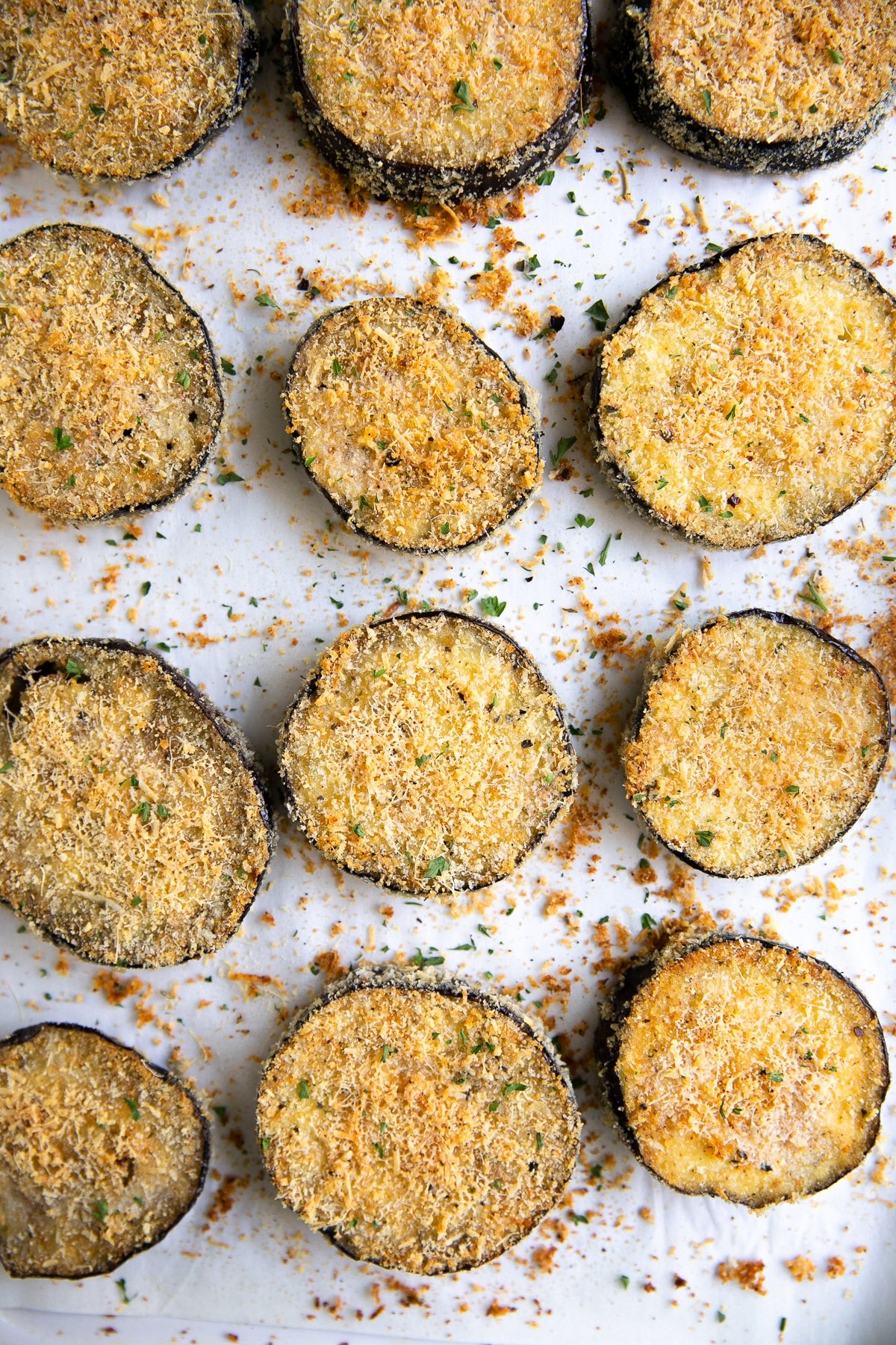 Crispy baked eggplant slices breaded with panko and parmesan cheese on a large baking sheet.