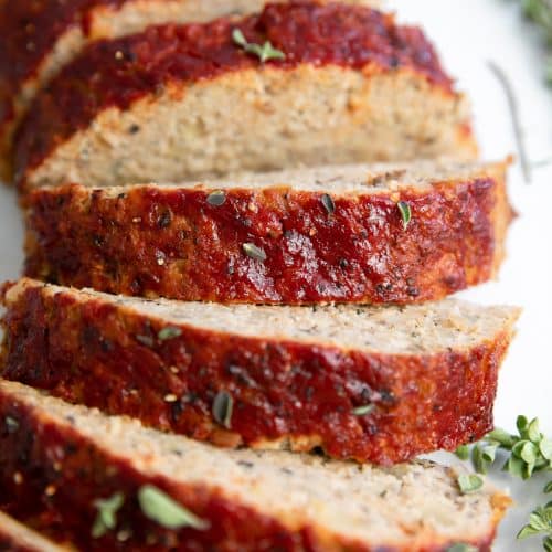 Close up image of large loaf of sliced turkey meatloaf made with ground turkey, chopped apples, and herbs.