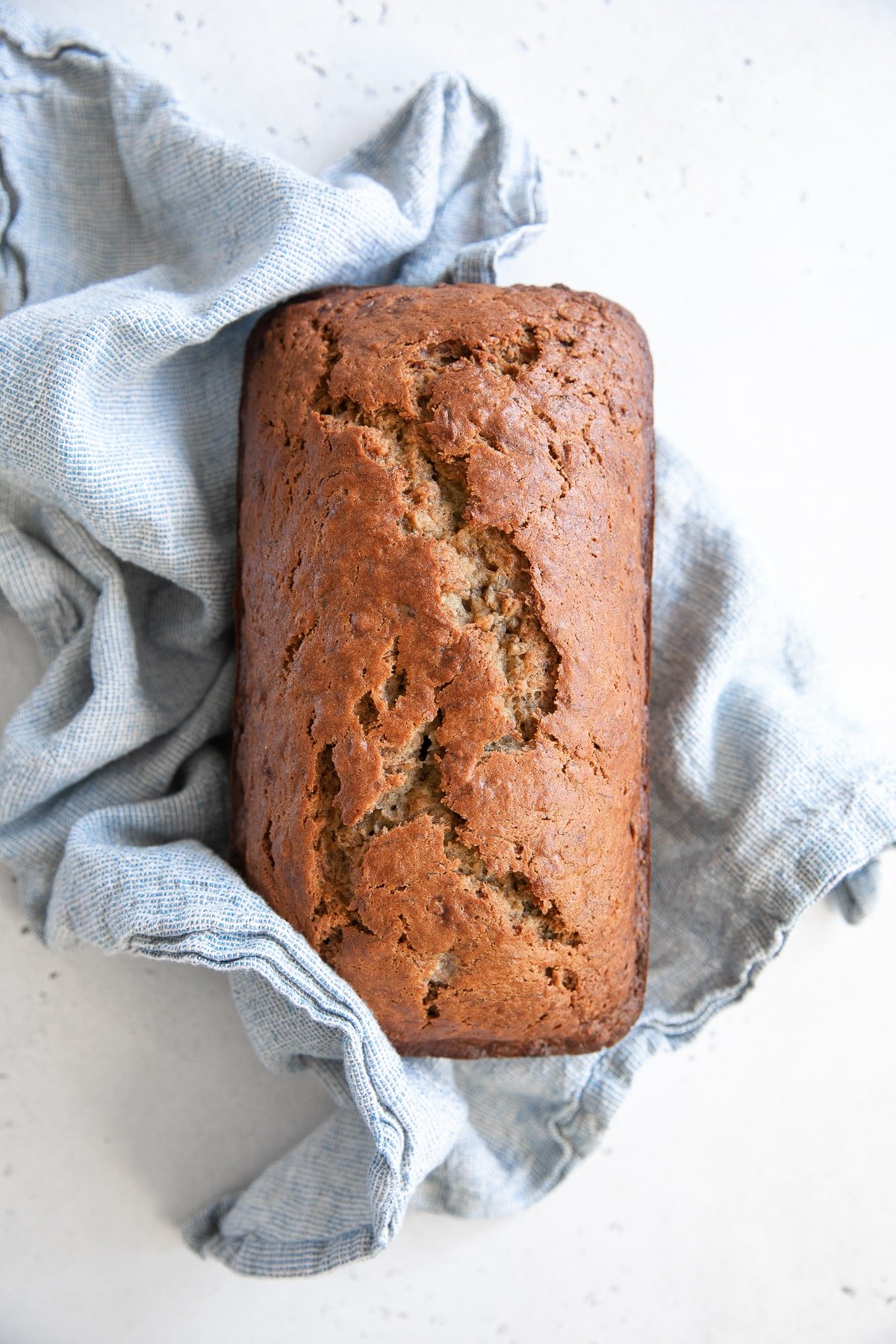 Fresh baked banana bread loaf wrapped in a light blue kitchen towel.