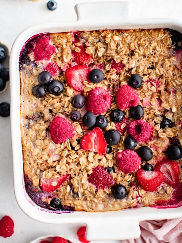Close-up of baked oatmeal topped with golden oats and baked berries in a white dish.