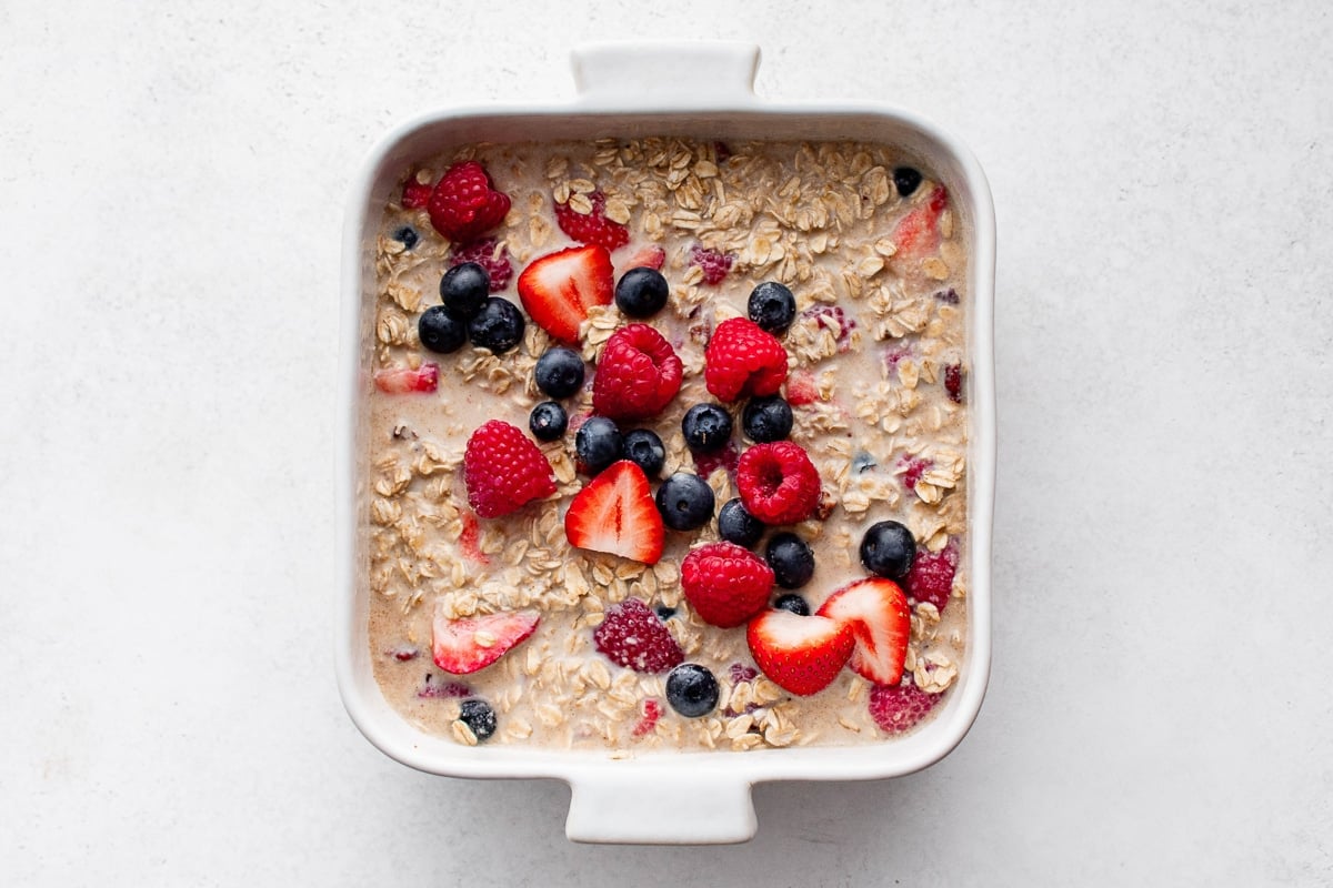 Oatmeal mixture in a baking dish topped with fresh strawberries, raspberries, and blueberries before baking.