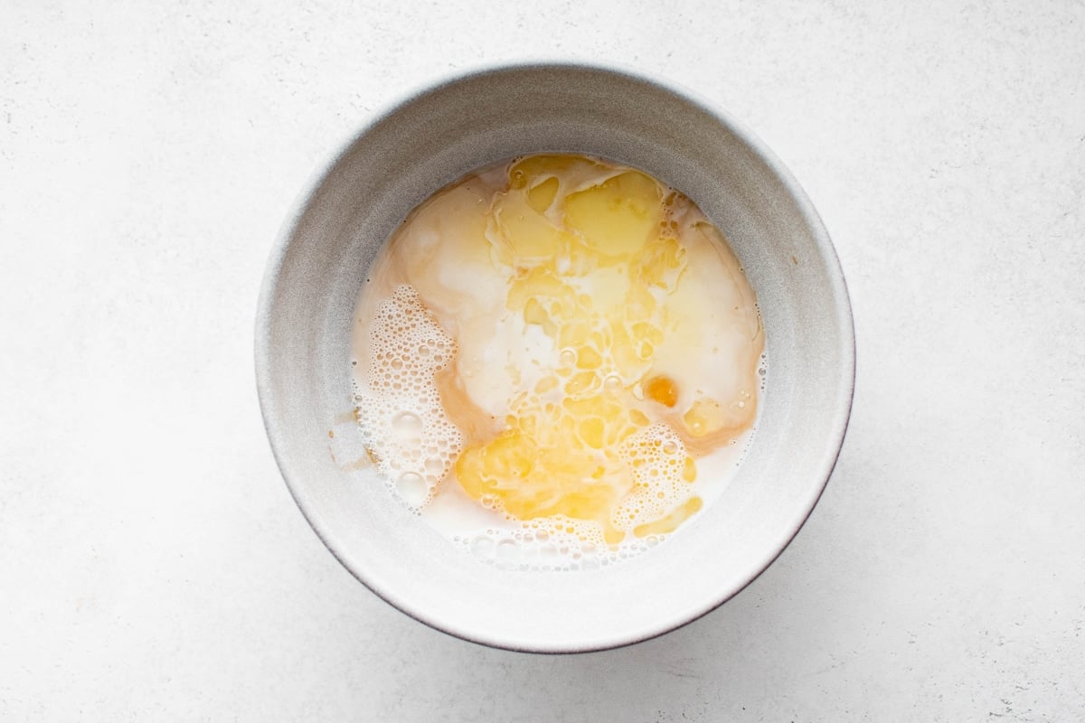 Milk, eggs, melted butter, and vanilla in a mixing bowl before being whisked together for baked oatmeal.